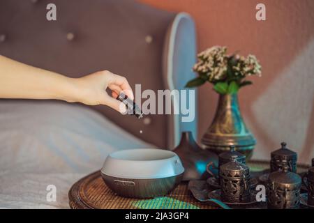 Frau, die ätherisches Öl in den Duftdiffusor auf dem Tisch gegeben hat Stockfoto