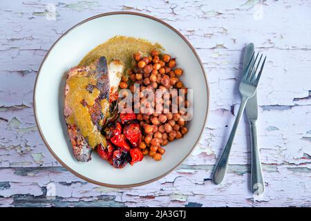 Ein frisch gekochtes Seebarsch-Filet, serviert mit gerösteten Tomaten und Kichererbsen. Eine gesunde, nahrhafte Mahlzeit mit hohem Gehalt an Omega-3-Fettsäuren Stockfoto