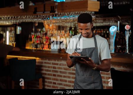 Afroamerikanischer Kellner, der im Restaurant auf einem digitalen Tablet arbeitet Stockfoto