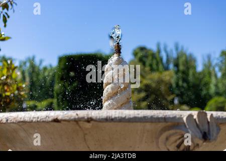 Brunnen. Steinbrunnen, gefüllt mit Wasser und einem Wasserstrahl an seiner Spitze in einem Park in Madrid an einem klaren Tag mit blauem Himmel, in Spanien. Europa. Foto Stockfoto