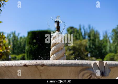 Brunnen. Steinbrunnen, gefüllt mit Wasser und einem Wasserstrahl an seiner Spitze in einem Park in Madrid an einem klaren Tag mit blauem Himmel, in Spanien. Europa. Foto Stockfoto