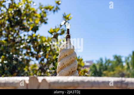 Brunnen. Steinbrunnen, gefüllt mit Wasser und einem Wasserstrahl an seiner Spitze in einem Park in Madrid an einem klaren Tag mit blauem Himmel, in Spanien. Europa. Foto Stockfoto