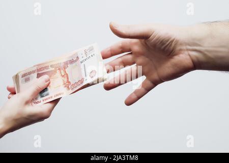 Die Handfläche eines Mannes greift nach einer Packung mit fünftausendsten Scheinen, die in der Hand einer Frau liegen. Stockfoto