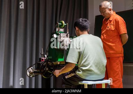 (220527) -- XINMI, 27. Mai 2022 (Xinhua) -- Cheng Yucai (R) führt einen Lehrling am 24. Mai 2022 in seiner Werkstatt in Xinmi, der zentralchinesischen Provinz Henan, zur Bedienung einer Guillochiermaschine. Guilloche ist eine dekorative Technik, bei der ein präzises, kompliziertes und sich wiederholendes Muster mechanisch durch Drehen des Motors in ein Material eingraviert wird. Die Technik verwendet eine Maschine, die von der Zartheit der Hand des Handwerkers gesteuert wird. Als ein wichtiger Prozess bei der Herstellung überlegener Uhren und Schmuck, wird die Kunst heute von selten wenigen Menschen gemeistert. Cheng Yucai, geboren 1978, lernte 2013 Guilloche kennen, als er ihn annahm Stockfoto