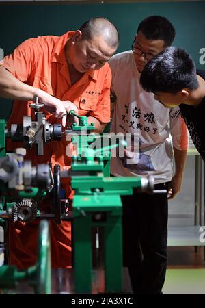 (220527) -- XINMI, 27. Mai 2022 (Xinhua) -- Cheng Yucai (L) erklärt seinen Auszubildenden am 24. Mai 2022 in seiner Werkstatt in Xinmi, der zentralchinesischen Provinz Henan, die Funktionsspezifikationen einer Guillochiermaschine. Guilloche ist eine dekorative Technik, bei der ein präzises, kompliziertes und sich wiederholendes Muster mechanisch durch Drehen des Motors in ein Material eingraviert wird. Die Technik verwendet eine Maschine, die von der Zartheit der Hand des Handwerkers gesteuert wird. Als ein wichtiger Prozess bei der Herstellung überlegener Uhren und Schmuck, wird die Kunst heute von selten wenigen Menschen gemeistert. Cheng Yucai, geboren 1978, kam nach kn Stockfoto