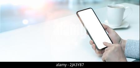 Mockup Handy. Frau drückt ihren Finger auf weißen Bildschirm des Mobiltelefons, während sie am Tisch im Café sitzt. Frau hält schwarzes Handy p Stockfoto