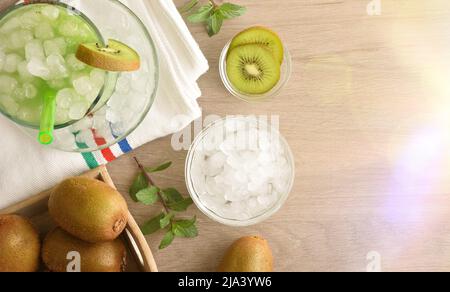 Kiwi kaltes Getränk auf Holztisch für den Sommer mit Obst und Schüssel mit zerkleinertem Eis. Draufsicht. Horizontale Zusammensetzung. Stockfoto