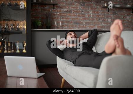 Lächelnder junger Mann, der auf der Couch liegt. Stockfoto