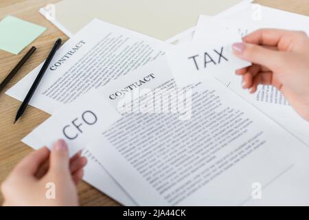 Beschnittene Ansicht einer Frau, die Papiere hält, mit Steuer- und cfo-Schriftzügen in der Nähe des Arbeitsverhältnisses auf dem Schreibtisch Stockfoto