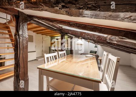 Zimmer im Dachgeschoss mit Esstisch aus Holz und Glasplatte, weißen Stühlen und restaurierten Vintage-Holzbalken Stockfoto