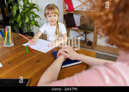 Glückliches lächelndes kleines Mädchen, das während außerschulischer Aktivitäten einen Therapeuten ansieht. Einzelunterricht im Zentrum der frühen Entwicklung der Kinder. Concep Stockfoto