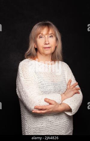 Porträt einer älteren Frau mit weißem Pullover auf schwarzem Hintergrund posiert Stockfoto