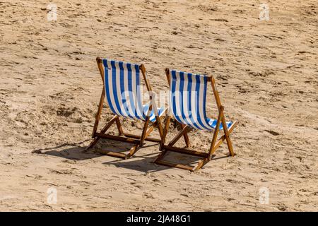 Zwei einsame blau-weiß gestreifte Liegestühle am Strand Stockfoto