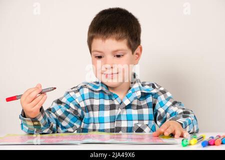 Ein Junge im Vorschulalter studiert und passiert Labyrinthe auf weißem Hintergrund. Vorbereitung für die Schule für Kinder. Stockfoto