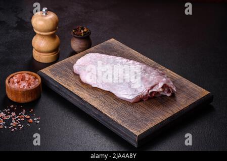 Frischer roher putenflügel mit Gewürzen und Kräutern auf einem Holzschneidebrett vor dunklem Betongrund. Zubereitung von Zutaten für Suppenpräparat Stockfoto