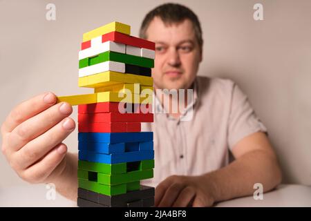 Ein Mann spielt ein Brettspiel, zieht vorsichtig mehrfarbige Blöcke aus dem Turm. Stockfoto