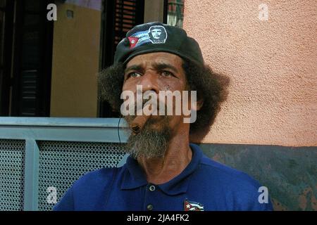 Bärtiger alter kubaner mit Che Guevara-Mütze, der eine große Zigarre raucht, Cathedral Plaza, historische Altstadt von Havanna, Kuba, Karibik Stockfoto