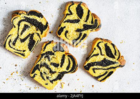 Ungewöhnliches Kürbis-Marmorbrot (Tiger-Print) mit Tintenfischfarbe, geflochten auf hellem Hintergrund. Nützliche Backwaren. Stockfoto