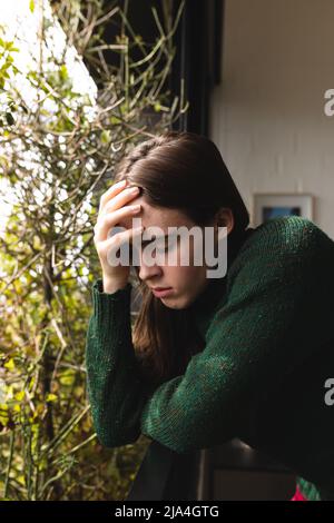 Gestresste nicht-binäre Trans-Frau, die ihren Kopf auf dem Balkon zu Hause hält Stockfoto