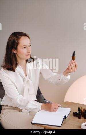 Das Aromatherapeutin-Mädchen sitzt in ihrem Büro und hält eine Flasche aromatisches Öl in den Händen und schreibt etwas auf. Es gibt ätherisches Öl Stockfoto