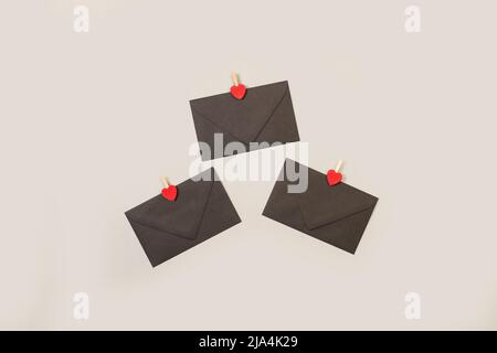 Schwarze Umschläge mit roten Herzen auf grauem Hintergrund Stockfoto