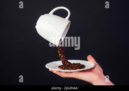 Magische Kaffeebohne spritzt aus einer Tasse mit Teller auf schwarzem Hintergrund Stockfoto