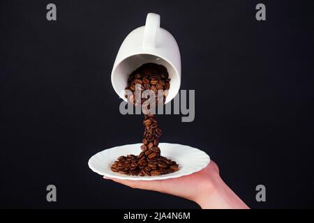 Magische Kaffeebohne spritzt aus einer Tasse mit Teller auf schwarzem Hintergrund Stockfoto