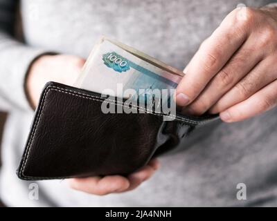 Hände nehmen Sie russische Rubel aus der Brieftasche. Nahaufnahme auf die Hände eines Menschen, wie er ist, eine Banknote aus seiner Brieftasche Stockfoto