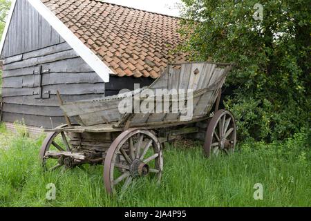 Ein Holzwagen steht im Gras vor dem Bauernhof Stockfoto