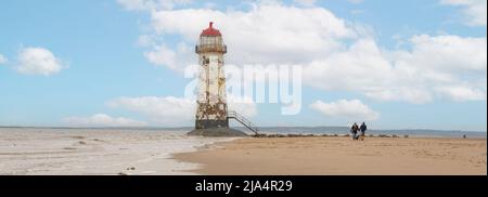 Talacre Beach-Flintshire, North Wales April 18 2022 Hundewanderer passieren den Ayr Lighthouse, während das Meer noch draußen ist Stockfoto