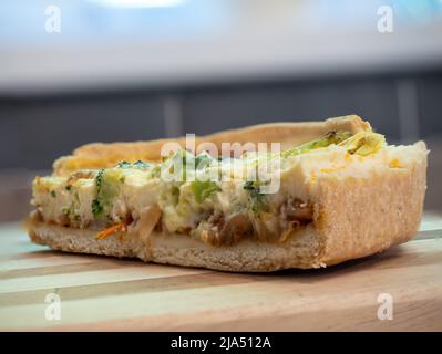 Ausgewählte Nahaufnahme einer Scheibe veganer vegetarischer Quiche mit Tomaten, Lauch und Brokkoli auf einer Holzplatte Stockfoto