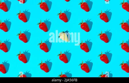 Muster aus reifen Erdbeeren auf pastellblauem Hintergrund mit einer unreifen Erdbeere. Minimales Sommerobstkonzept. Isometrische flache Ablage. Stockfoto
