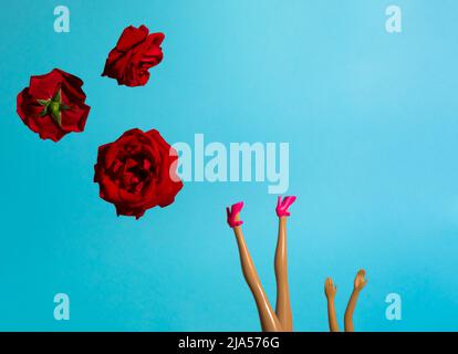 Kreatives Arrangement mit roten Rosen und Puppenbeinen in High Heels vor himmelblauem Hintergrund. Minimales Sommerkonzept. Valentinstag oder 8 März Idee. Stockfoto