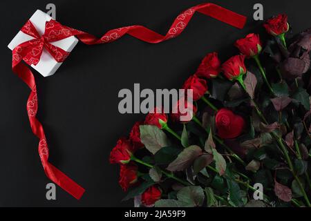 Rote Rosen und Geschenkbox auf schwarzem Hintergrund Stockfoto