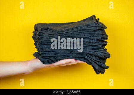 Ein Stapel frischer neuer schwarzer Socken in der Hand auf gelbem Hintergrund Stockfoto