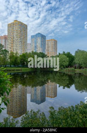 Mehrstöckige Wohngebäude spiegeln sich in blauem Wasser vor dem Hintergrund des blu-Himmels. Schöne Aussicht auf die Wohnanlage parkovi Stockfoto