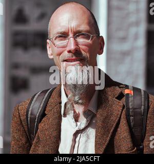 Ein Mann mit einem grauen Spitzbart in einer orangefarbenen Tweed-Jacke hält in Truro, Cornwall, für ein Straßenportrait in der Sonne an. Stockfoto