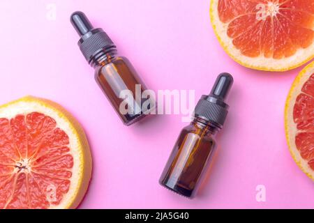 Ätherisches Grapefruitöl mit frischen Grapefruitscheiben und zwei glasbraunen Flaschen mit schwarzer Pipette Stockfoto