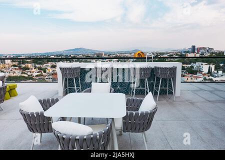 Vom Dach eines neuen Apartmentkomplexes in Jardines del Bosque, Guadalajara, Mexiko, blicken Sitzplätze und ein Tisch auf die Skyline Stockfoto