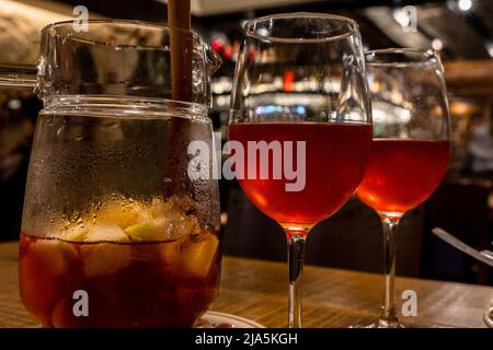 Ein Krug mit Sangria, begleitet von zwei Gläsern, die auf einem Holztisch aufgestellt sind. Stockfoto