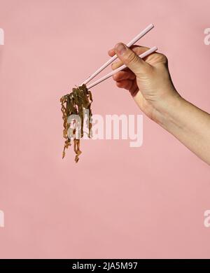 Frauenhand mit Essstäbchen mit Laminaria auf farbigem Hintergrund Stockfoto