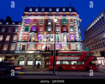Das Kaufhaus Fortnum und Mason liegt nachts auf Piccadilly, wenn ein Bus durch die lange Belichtung verschwommen vorbeifährt. London. Stockfoto