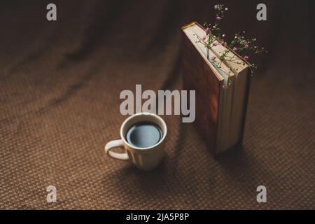 Ein Buch mit Blumen und einer Tasse Kaffee auf dunklem Hintergrund von oben Stockfoto