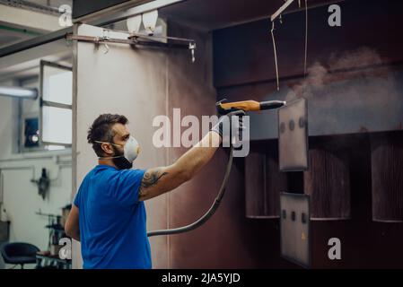 Der Maler malt das Eisen-Element. Teile für die industrielle Lackierung. Metalldesigns Stockfoto