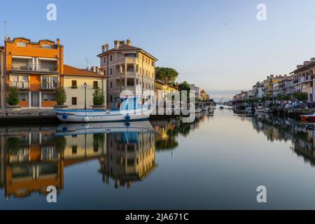 Grado, Italien - 8. Juli 2021: Der chanel in der Touristenstadt Grado in der morgendlichen goldenen Stunde mit Gebäuden und Reflexionen im Wasser Stockfoto