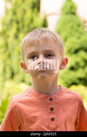 Fünfjähriger Junge, der Gesichter macht. Ein fünfjähriger blonder Junge macht Gesichter, während er bei sonnigem Wetter auf der Straße steht Stockfoto