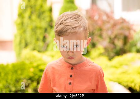 Fünfjähriger Junge, der Gesichter macht. Ein fünfjähriger blonder Junge macht Gesichter, während er bei sonnigem Wetter auf der Straße steht Stockfoto