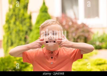 Fünfjähriger Junge, der Gesichter macht. Ein fünfjähriger blonder Junge macht Gesichter, während er bei sonnigem Wetter auf der Straße steht Stockfoto