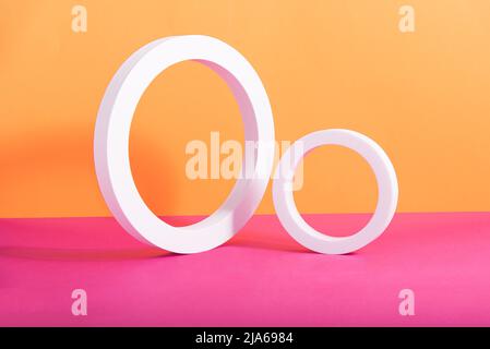 Abstrakte geometrische Komposition aus zwei weißen kreisförmigen Rahmen auf orangefarbenem und pinkem Hintergrund. Hintergrundbild. Rechteckig mit Kopierbereich. Isometrisch. Stockfoto