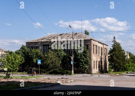 Bakhmut, Ukraine. 24.. Mai 2022. Ein Mann fährt mit dem Fahrrad an einem Wohnhaus mit einem Dach vorbei, das durch Schüsse in Bakhmut, Donbas, beschädigt wurde. Da Bakhmut als Schlüsselstadt der ukrainischen Streitkräfte bei der Verteidigung der Donezker Region steht, wird die Stadt von russischen Truppen angegriffen. Die russische Invasion der Ukraine begann am 24. Februar, dem Krieg, der zahlreiche Zivilisten und Soldaten getötet hat. Kredit: SOPA Images Limited/Alamy Live Nachrichten Stockfoto